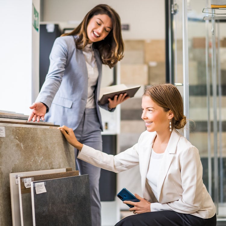 A female employee in a tiling store showing a customer tiles and great prices.