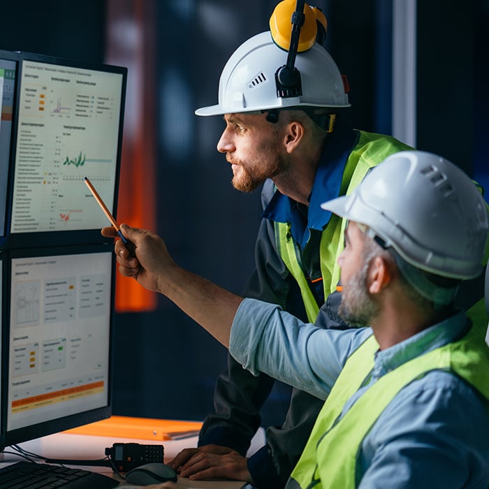 Two employees managing complex products while viewing data on a digital screen