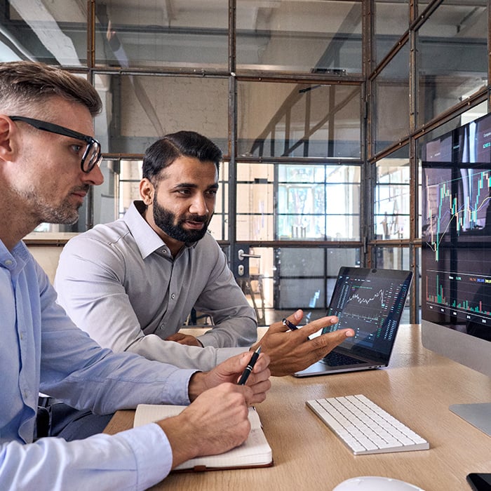 Two men looking at data together on multiple screens.